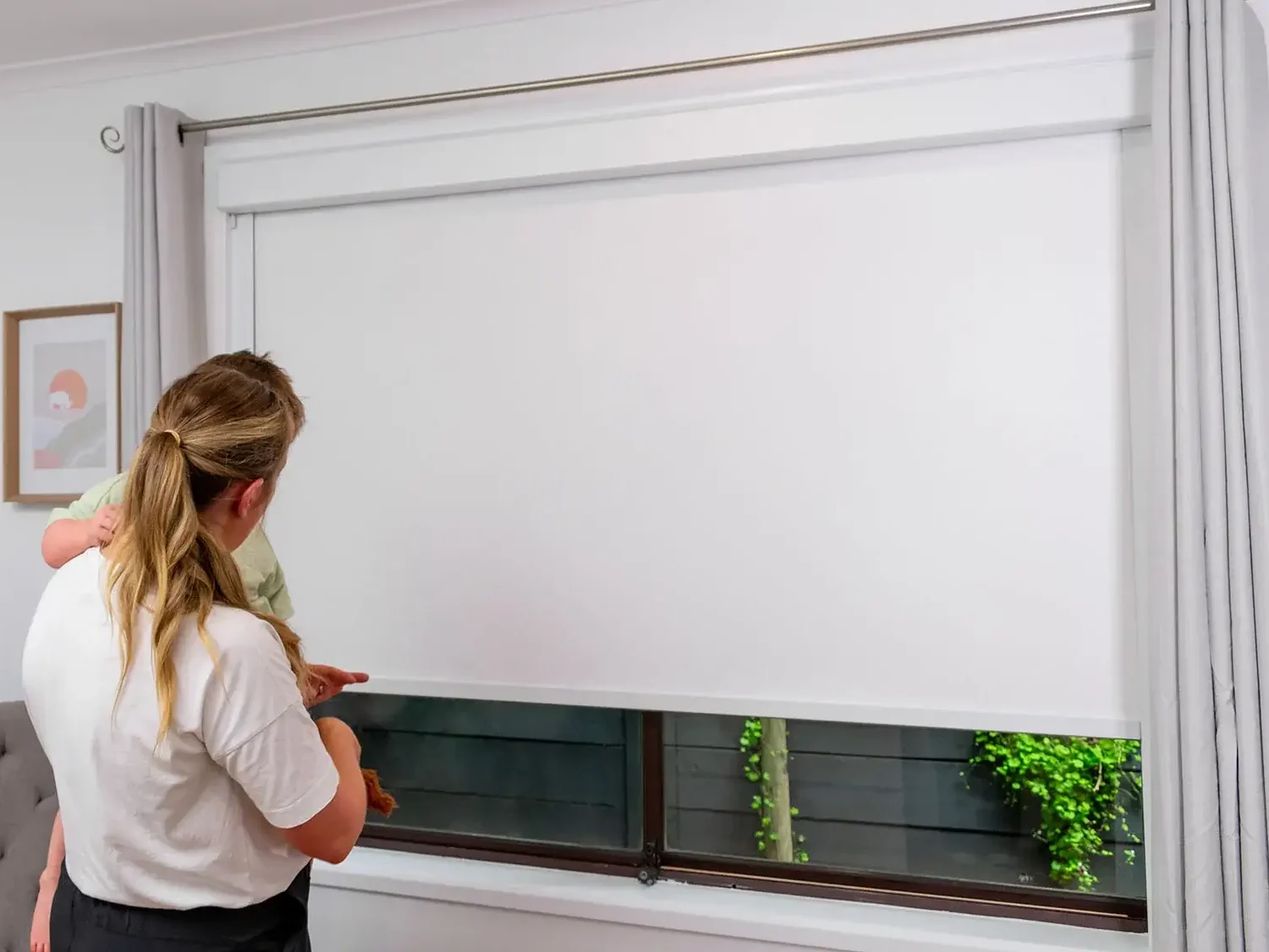 woman holding a child looking at a window with interior blinds