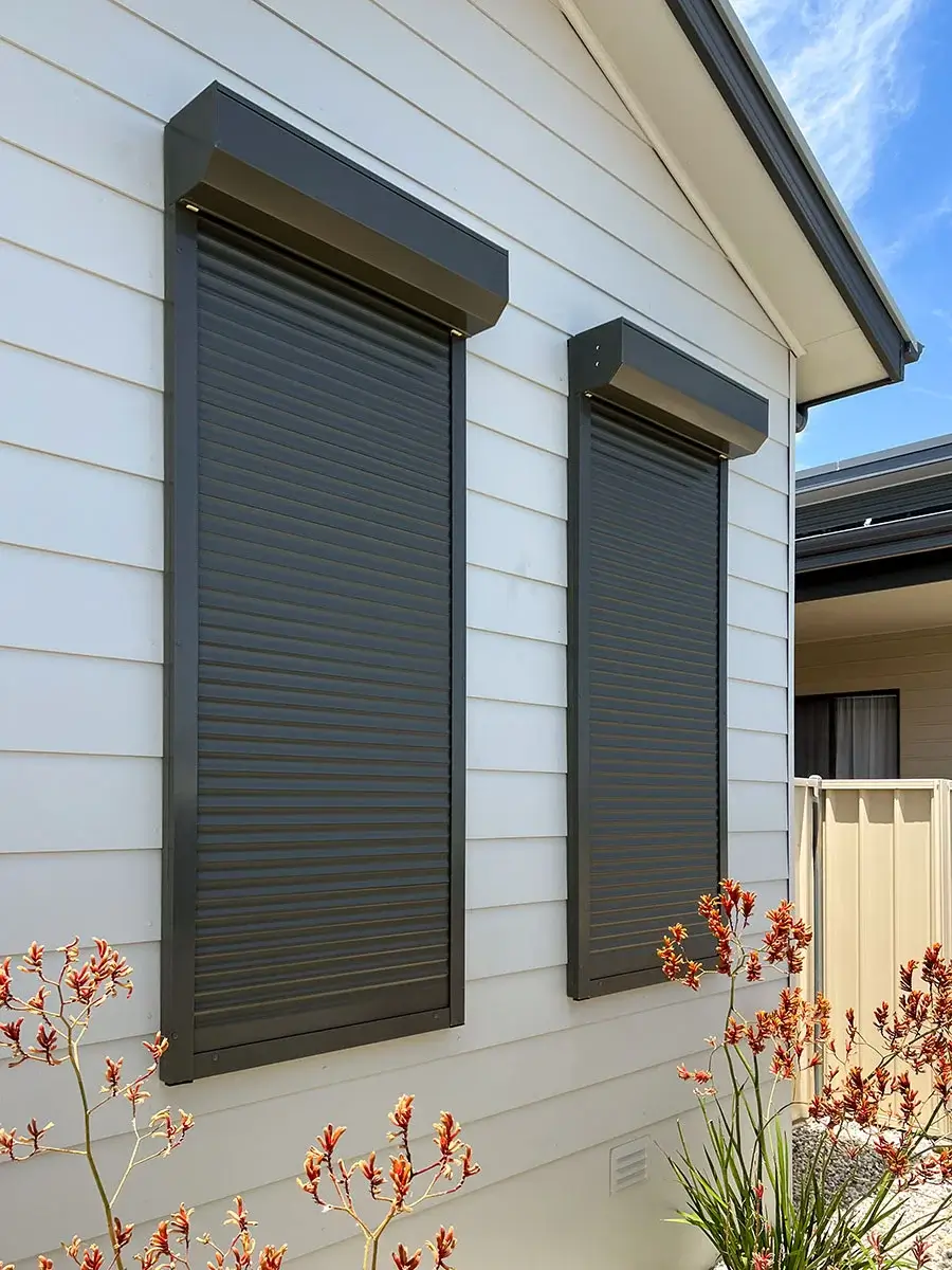 Two black roller shutters on a white weatherboard home