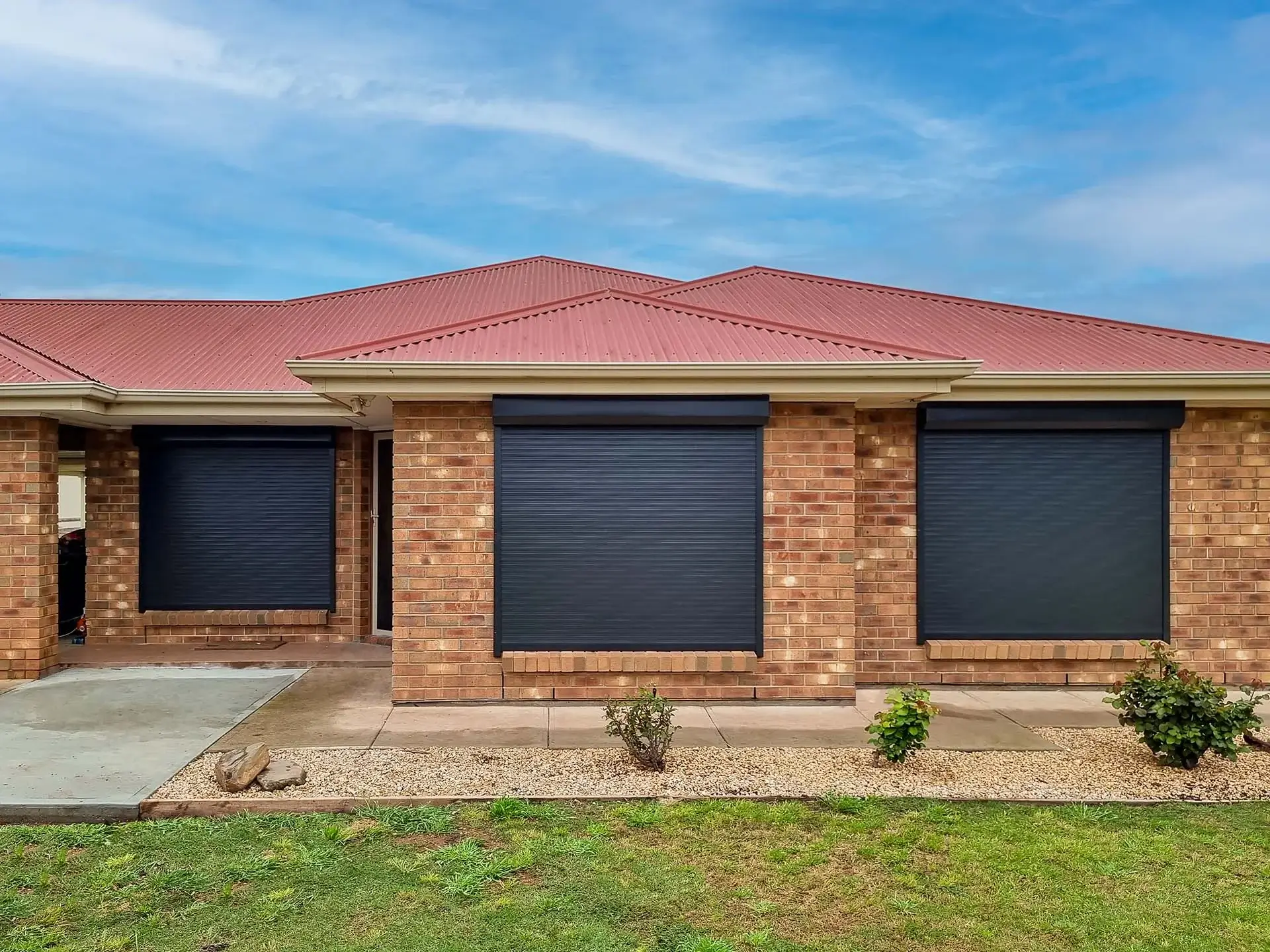 a brick home with three black roller shutters on the windows