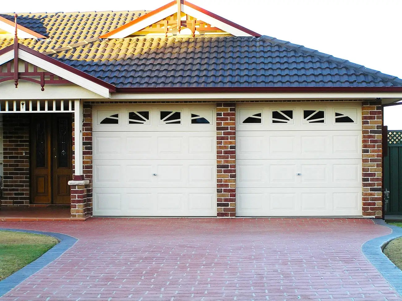 Brick house with a double panel lift garage door featuring decorative windows, set against a paved driveway leading to the front entrance.