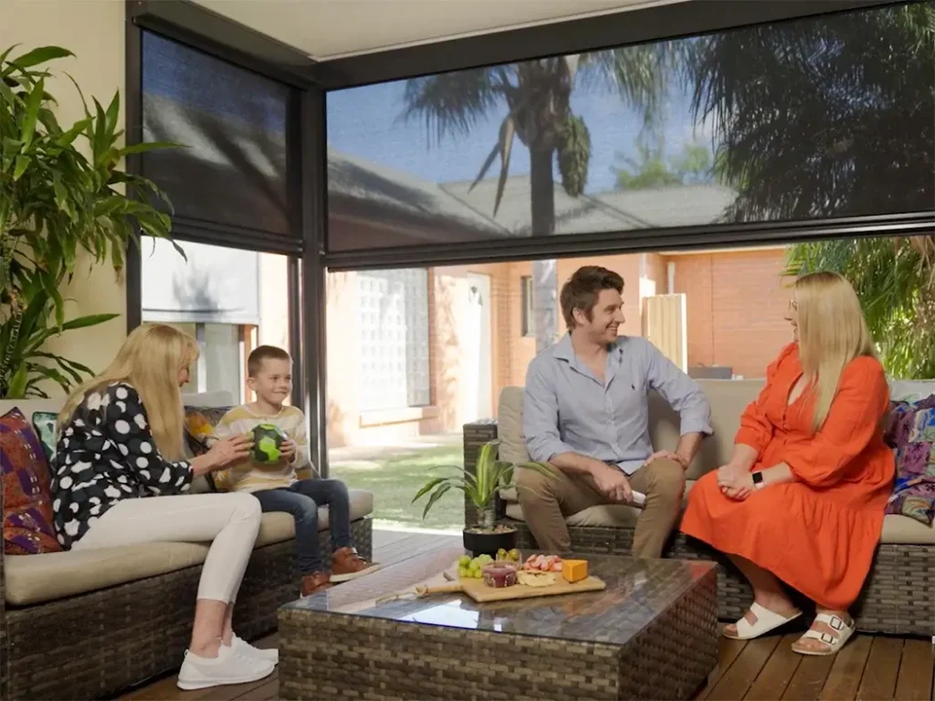 Family sitting together in a cosy enclosed patio area, enjoying snacks and conversation, with outdoor blinds providing shade and privacy.
